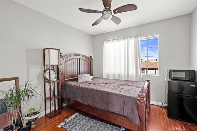 bedroom featuring baseboards, ceiling fan, wood finished floors, and refrigerator