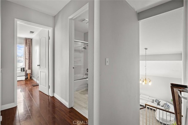 hall featuring a chandelier, visible vents, baseboards, and wood finished floors