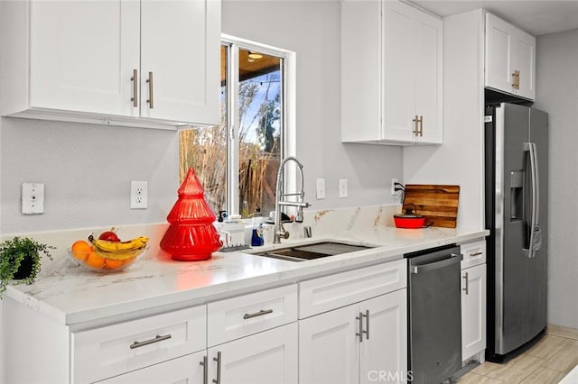 kitchen featuring light stone counters, appliances with stainless steel finishes, white cabinets, and a sink