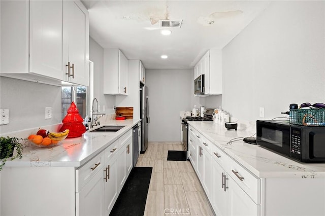 kitchen with stainless steel appliances, white cabinets, a sink, and visible vents