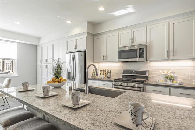 kitchen featuring appliances with stainless steel finishes, a breakfast bar, light stone counters, and sink