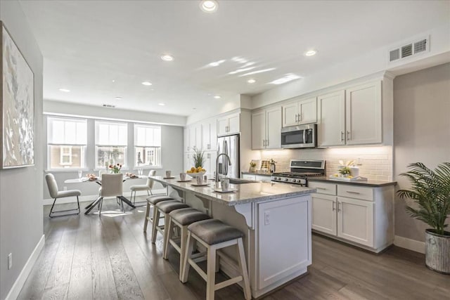 kitchen with a center island with sink, appliances with stainless steel finishes, dark hardwood / wood-style floors, sink, and white cabinetry