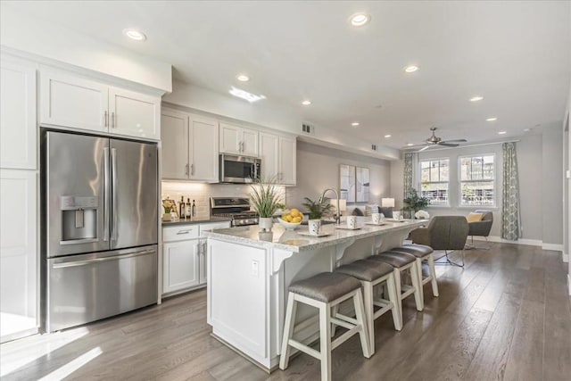 kitchen featuring stainless steel appliances, an island with sink, a breakfast bar area, white cabinets, and ceiling fan