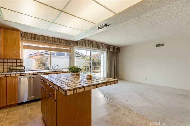 kitchen with a center island, tile counters, sink, light colored carpet, and stainless steel dishwasher