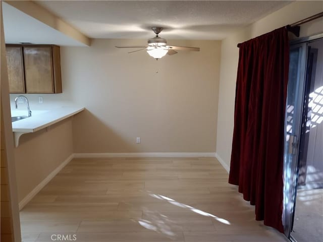 unfurnished dining area featuring ceiling fan, sink, a textured ceiling, and light hardwood / wood-style floors