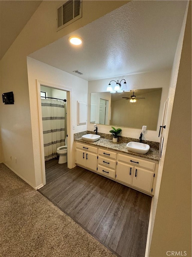 bathroom with toilet, ceiling fan, wood-type flooring, a textured ceiling, and vanity