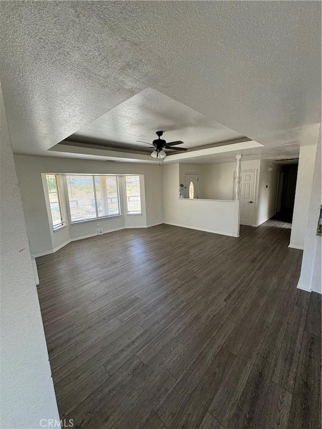 unfurnished living room with ceiling fan, a textured ceiling, dark hardwood / wood-style floors, and a raised ceiling