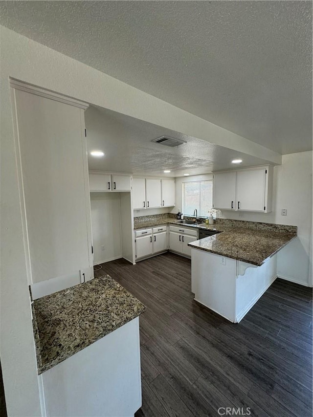 kitchen featuring a textured ceiling, kitchen peninsula, dark stone countertops, and white cabinets