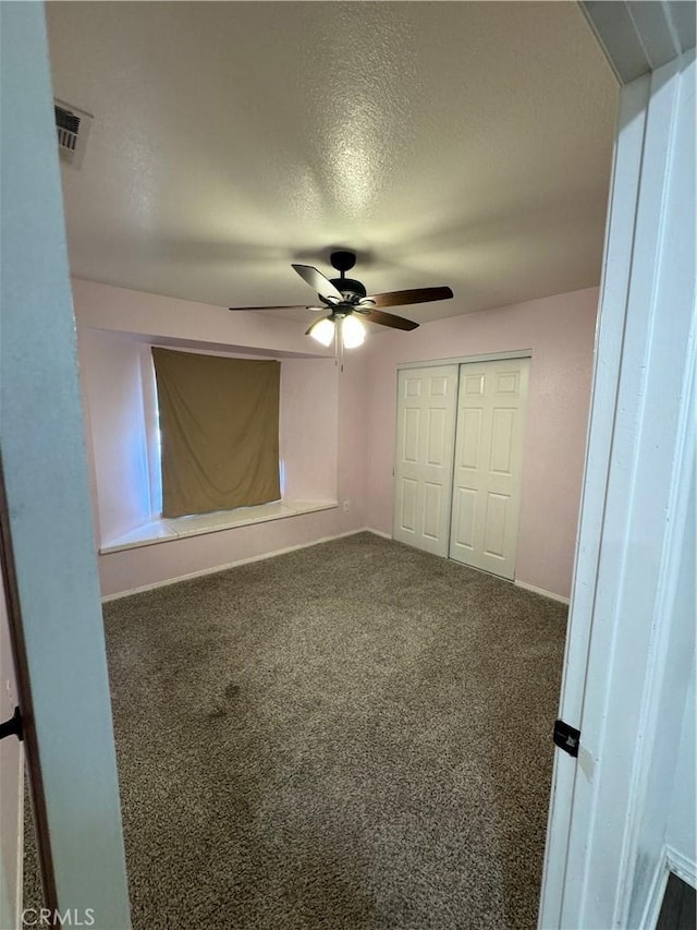 unfurnished bedroom with ceiling fan, a closet, dark carpet, and a textured ceiling