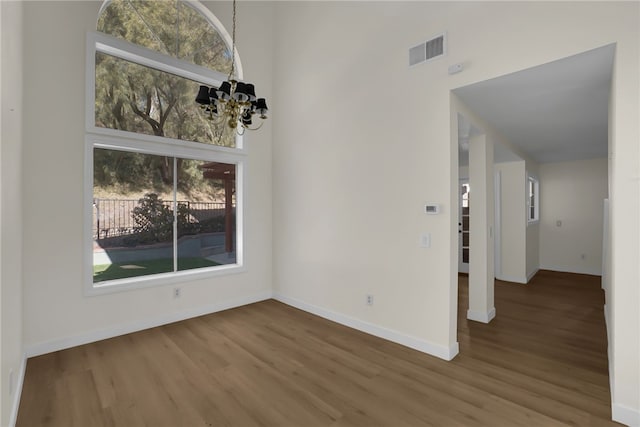 unfurnished room featuring a high ceiling, wood-type flooring, a chandelier, and a healthy amount of sunlight