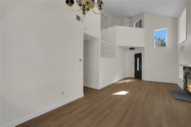 unfurnished living room with a high ceiling, an inviting chandelier, and wood-type flooring