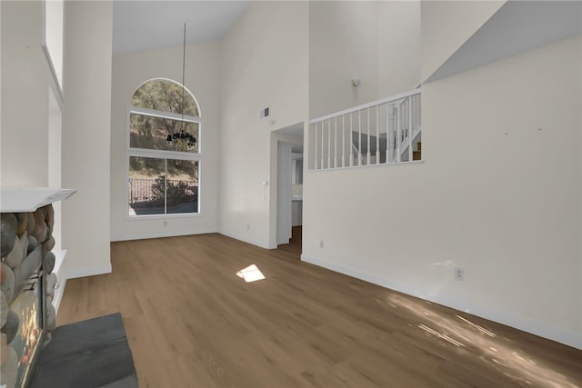 unfurnished living room featuring a stone fireplace, high vaulted ceiling, and wood-type flooring