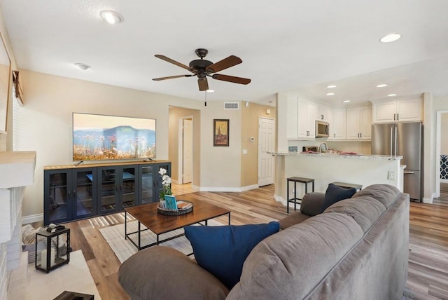 living room with sink, light wood-type flooring, and ceiling fan