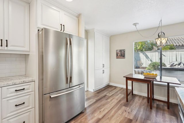 kitchen featuring stainless steel refrigerator, pendant lighting, light stone counters, decorative backsplash, and white cabinets