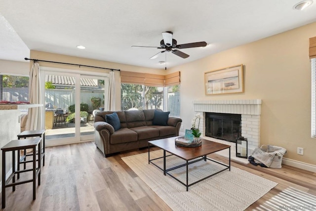 living room featuring ceiling fan, light wood-type flooring, and a brick fireplace