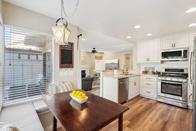 kitchen with kitchen peninsula, decorative light fixtures, stainless steel appliances, white cabinets, and sink