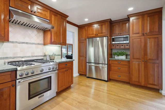 kitchen with light stone countertops, light hardwood / wood-style flooring, tasteful backsplash, appliances with stainless steel finishes, and ventilation hood