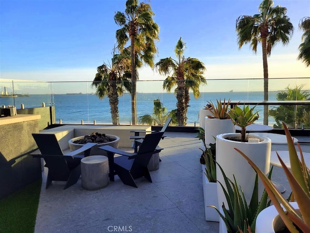 patio terrace at dusk featuring a water view, an outdoor fire pit, and a balcony