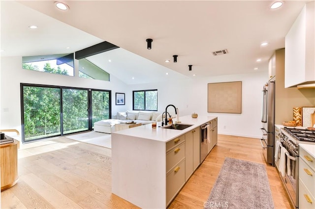 kitchen featuring high end appliances, light hardwood / wood-style flooring, sink, an island with sink, and vaulted ceiling with beams