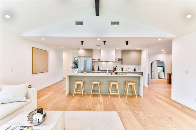 kitchen with a breakfast bar, tasteful backsplash, a kitchen island with sink, high quality fridge, and vaulted ceiling with beams