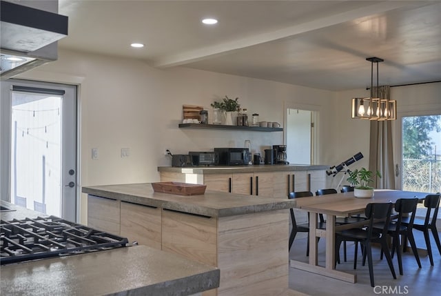 kitchen with light brown cabinetry, cooktop, a chandelier, and pendant lighting