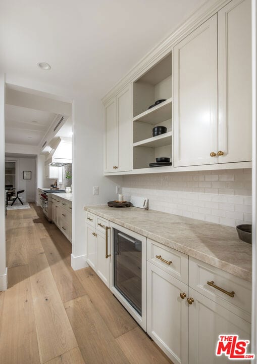 kitchen featuring white cabinetry, light stone counters, light hardwood / wood-style flooring, beverage cooler, and backsplash