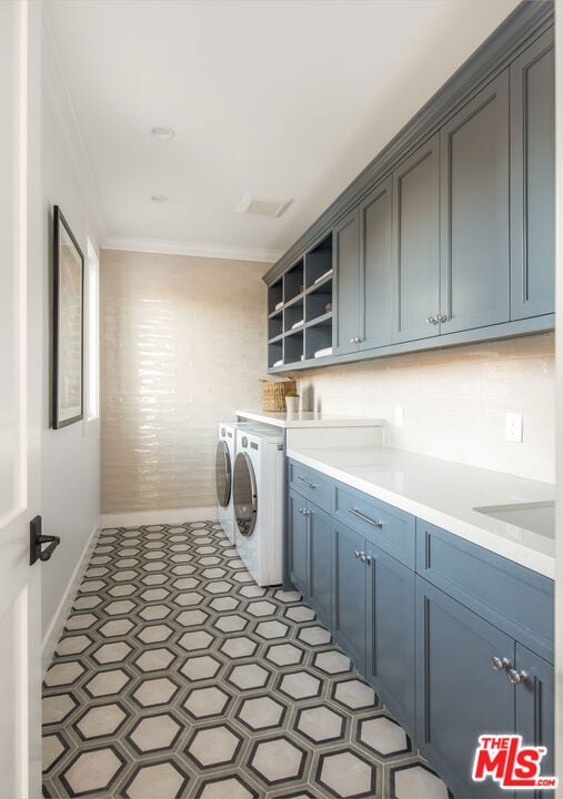 clothes washing area featuring cabinets, washing machine and clothes dryer, crown molding, and sink