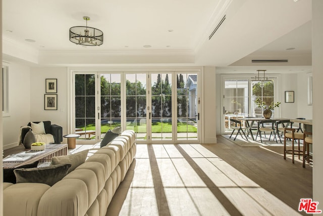 living room featuring a notable chandelier, a tray ceiling, crown molding, and wood-type flooring