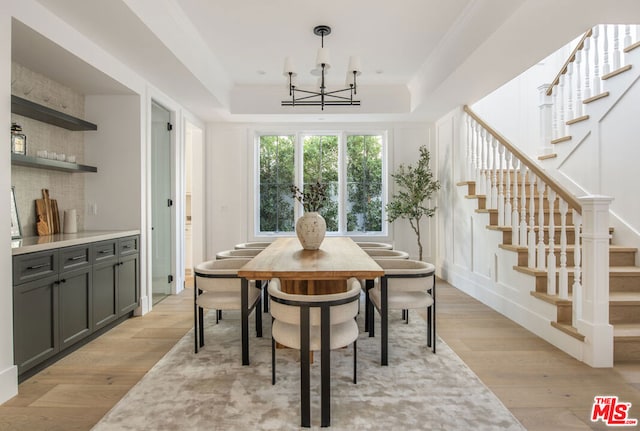 dining room featuring a raised ceiling, a chandelier, and light hardwood / wood-style floors