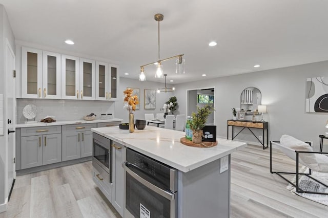 kitchen with light hardwood / wood-style flooring, pendant lighting, a center island, stainless steel appliances, and gray cabinets