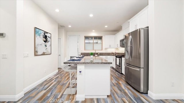 kitchen with dark hardwood / wood-style floors, a center island, stainless steel appliances, white cabinetry, and a kitchen breakfast bar