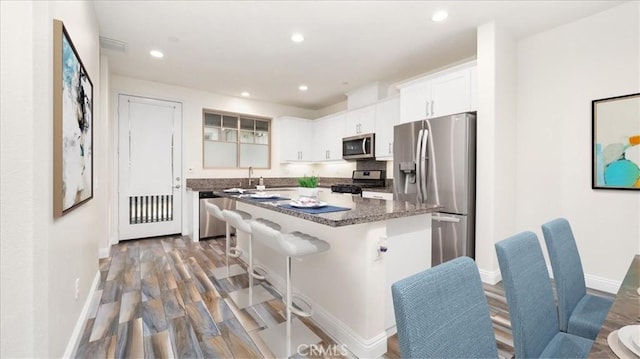 kitchen with a center island, a breakfast bar, dark hardwood / wood-style flooring, white cabinetry, and appliances with stainless steel finishes