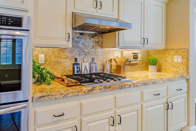 kitchen featuring white cabinets, light stone counters, decorative backsplash, ventilation hood, and appliances with stainless steel finishes