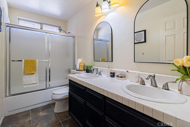 full bathroom featuring toilet, bath / shower combo with glass door, a textured ceiling, and vanity