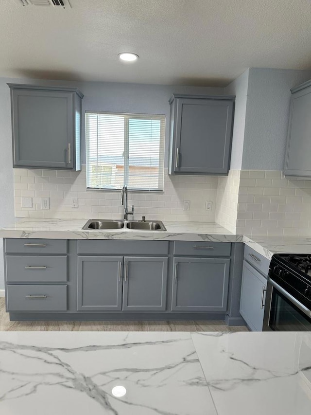 kitchen featuring stainless steel gas stove, gray cabinets, a textured ceiling, sink, and tasteful backsplash