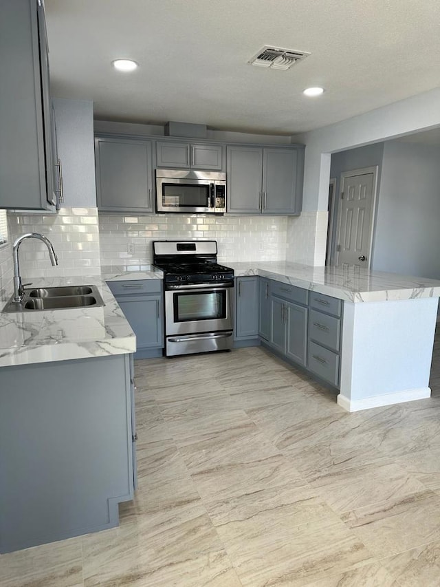 kitchen featuring gray cabinetry, stainless steel appliances, light stone countertops, kitchen peninsula, and sink