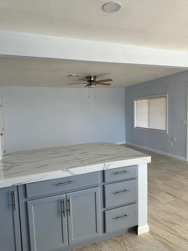 kitchen featuring a textured ceiling, ceiling fan, light stone counters, and gray cabinets