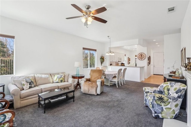 living room with ceiling fan with notable chandelier and light colored carpet