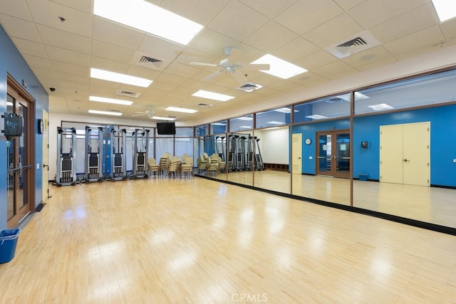 gym with ceiling fan, a paneled ceiling, light wood-type flooring, and french doors