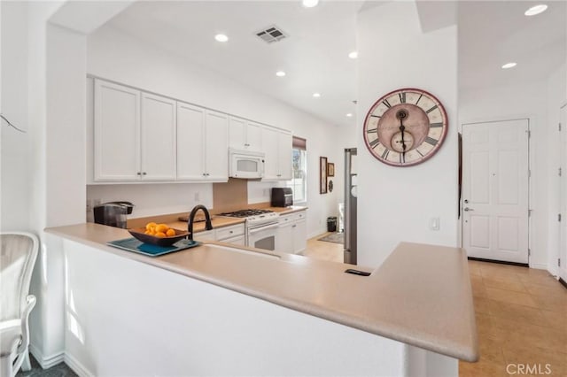 kitchen featuring white appliances, kitchen peninsula, light tile patterned floors, and white cabinets