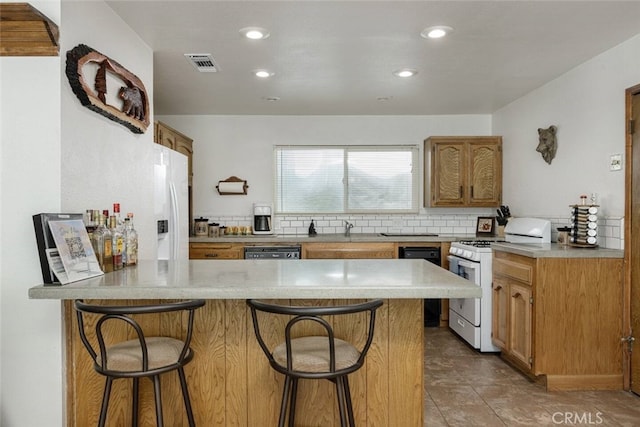 kitchen with white appliances, kitchen peninsula, tasteful backsplash, a kitchen bar, and sink