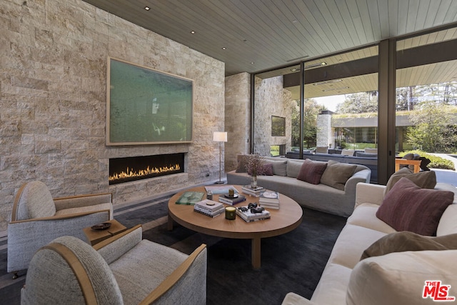 living room with a wall of windows, wooden ceiling, and an outdoor stone fireplace