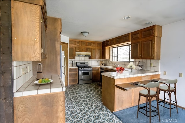 kitchen featuring a kitchen breakfast bar, gas stove, kitchen peninsula, tile countertops, and sink