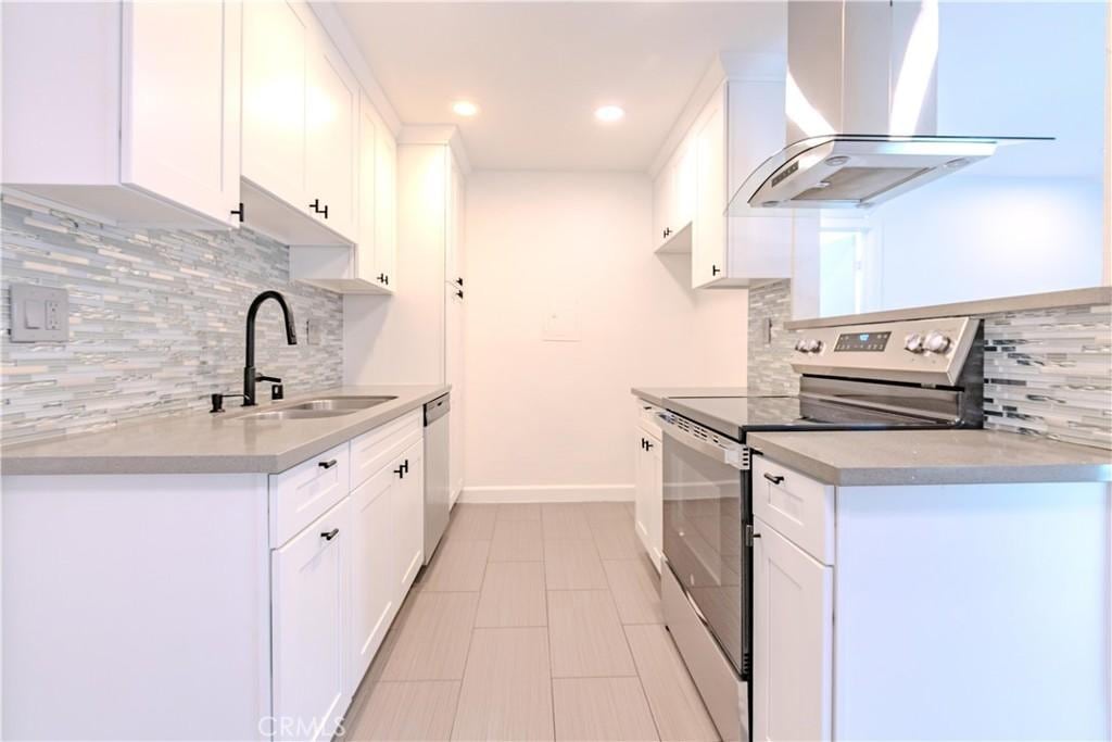 kitchen with backsplash, sink, white cabinetry, appliances with stainless steel finishes, and island range hood