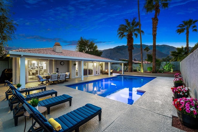 pool at dusk featuring a patio and a mountain view