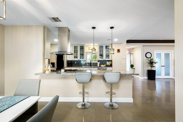 kitchen with island exhaust hood, a breakfast bar area, pendant lighting, light stone counters, and tasteful backsplash