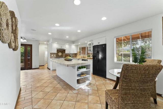 kitchen with light tile patterned flooring, a kitchen island, white cabinetry, decorative backsplash, and black fridge with ice dispenser