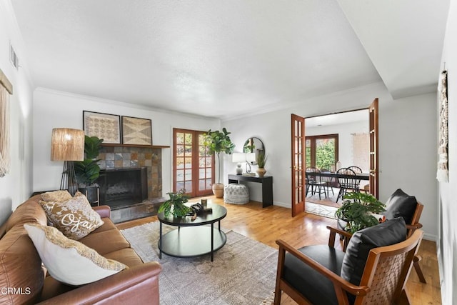 living room with a fireplace, light hardwood / wood-style flooring, ornamental molding, and french doors