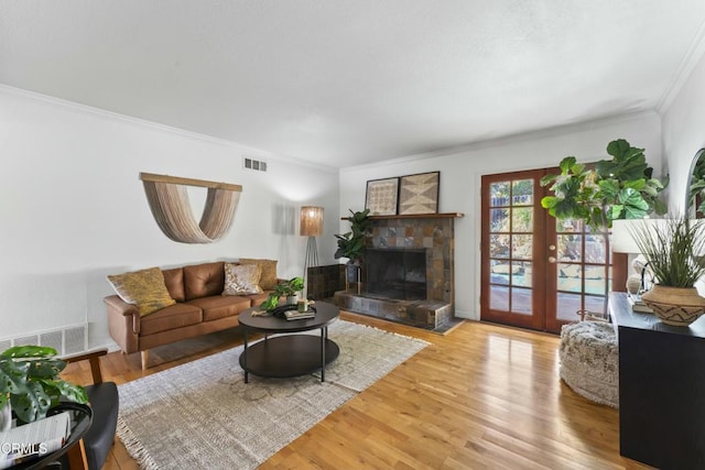 living room featuring crown molding, a stone fireplace, light wood-type flooring, and french doors