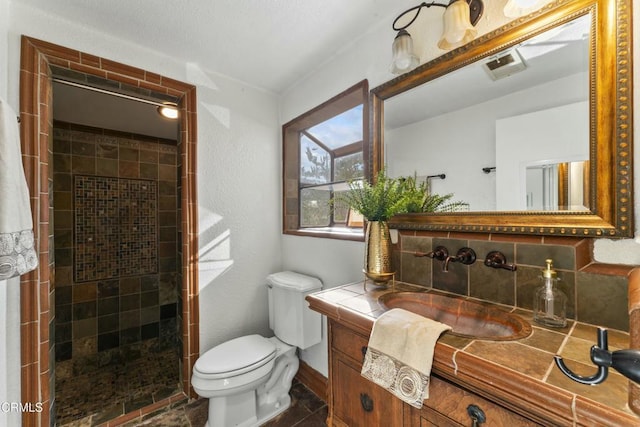 bathroom with vanity, a tile shower, decorative backsplash, and toilet